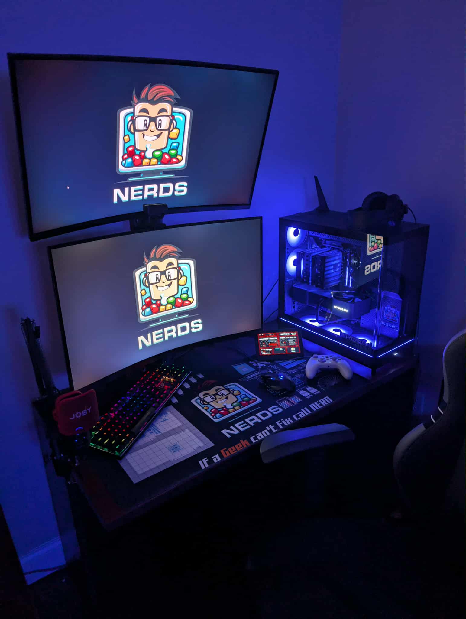 Dual monitor gaming desk setup with blue ambient lighting and NERDS branded desk mat